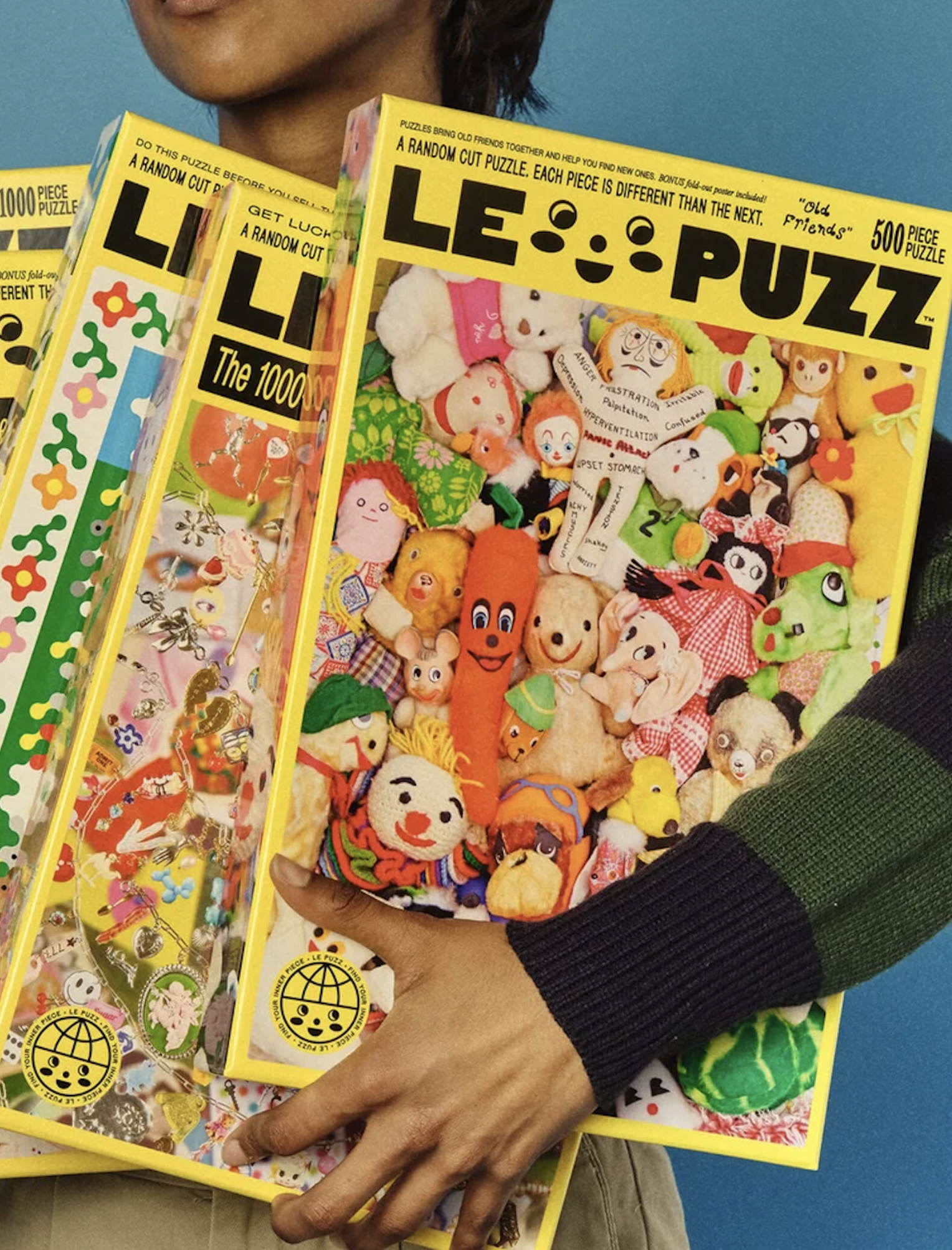 Person holding a stack of yellow Le Puzz jigsaw puzzle boxes